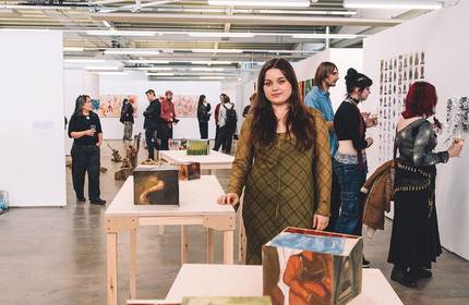 A woman stands in front of an art display, observing the various pieces with interest and contemplation.