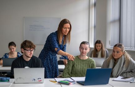 A lecturer points to the laptop of a student sat at a row of desks during a seminar