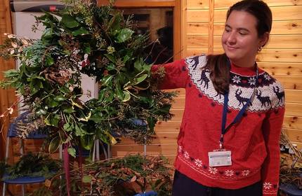 A young woman in a Christmas jumper holds a large wreath