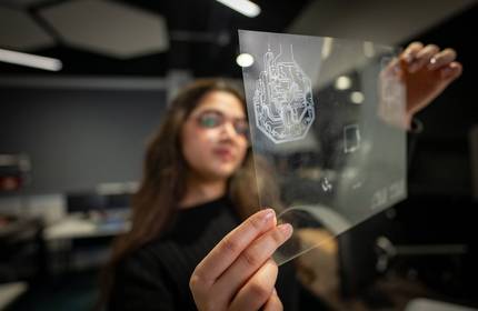 A person holds a small transparent sheet, etched with electronic circuits.