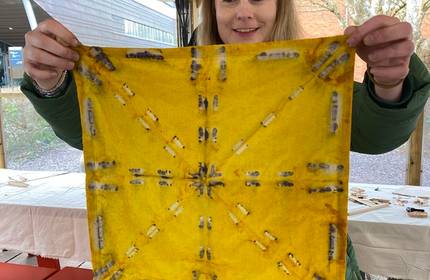 A young woman holds up a dyed yellow cloth