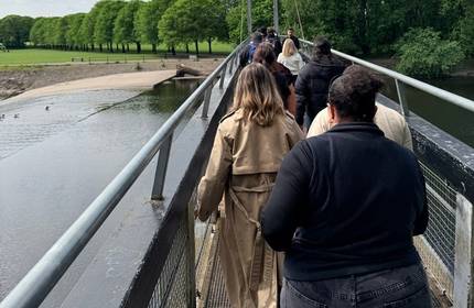 A group walk across a bridge over water during a sunny day