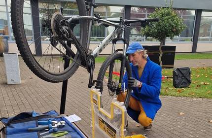A man works on a bicycle on a raised platform, with a row of tools laid out nearby