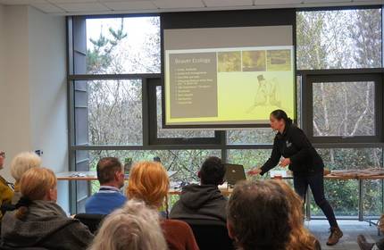 A woman reaches over to a laptop during a presentation in front of a busy room