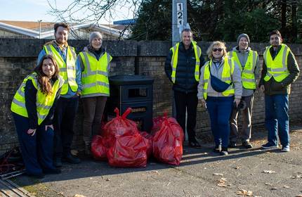A group of individuals in high-visibility jackets pose for a photograph with a collection of red litter bags
