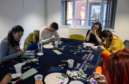 A small group of people painting small trinkets around a large table