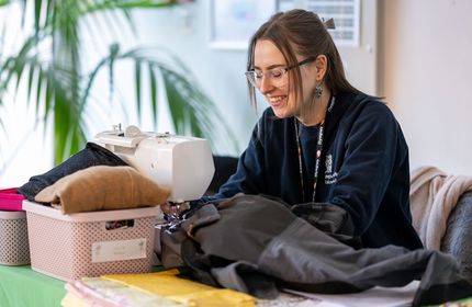 A member of Cardiff Met staff works at a sewing machine to repair clothing