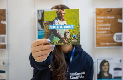 Cardiff Met staff member holds a Fairtrade information leaflet in front of their face