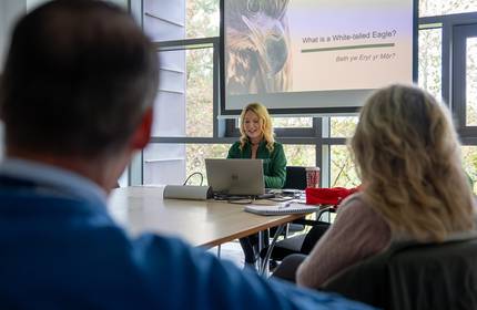 A woman sits at the head of a table leading a presentation