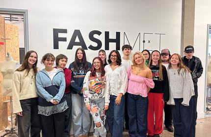 Group of fashion students and an instructor posing in front of a “FASHMET” wall.