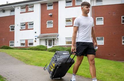 A student pulling a suitcase along a path, heading towards his student accommodation.