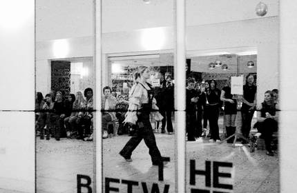 A black and white image of a mirror in which the reflection of a catwalk fashion show with attendees can be seen