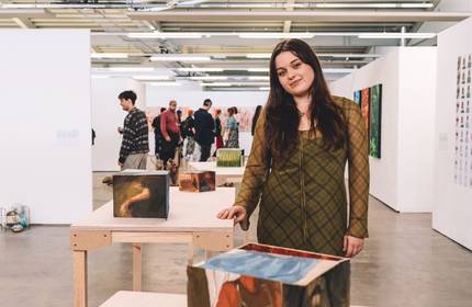 A woman stands in front of an art display, observing the various pieces with interest and contemplation.