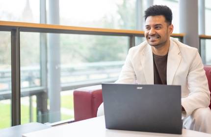 A man in a white jacket is comfortably positioned on a red couch, using a laptop, reflecting a blend of style and concentration.