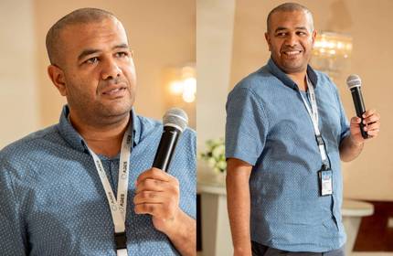 A man wearing a blue short-sleeved shirt holding a microphone.