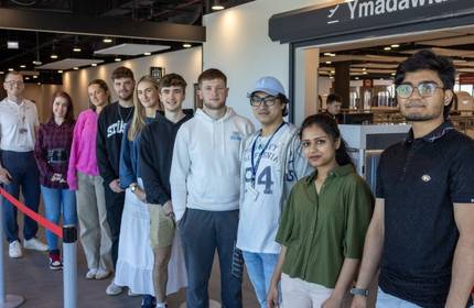 A group of young adults pose for a photograph in a bright open building
