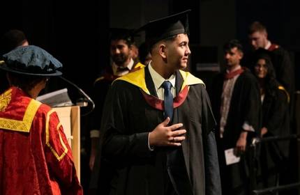 A student in graduation cap and gown walks across the stage during their graduation ceremony