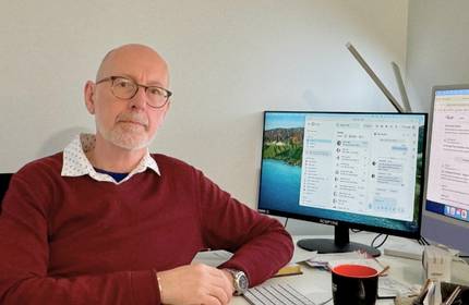 A bald man works at a desk with two computer monitors, engaged in tasks in a professional environment.