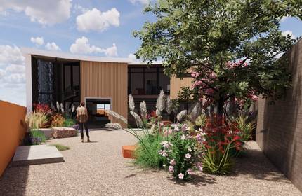 A modern house with a curved roof, large glass windows, and wood panelling, surrounded by a landscaped garden. A person walks along a gravel path, with colourful flowers and a tree in the foreground under a partly cloudy sky.