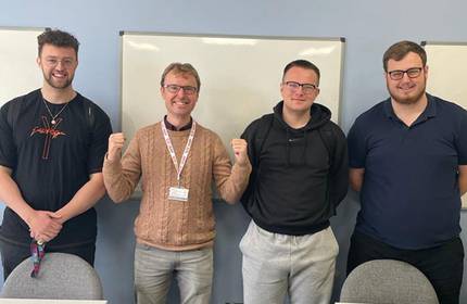 Four individuals stand for a photograph in a lecture room