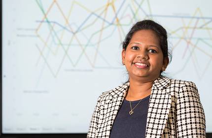 Merlin wearing a top and suit jacket, stands in front of a presentation board displaying a complex graph