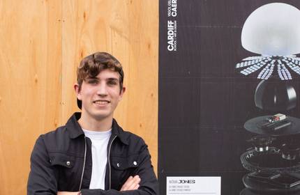 A young man stands beside a poster featuring a stylish lamp design.
