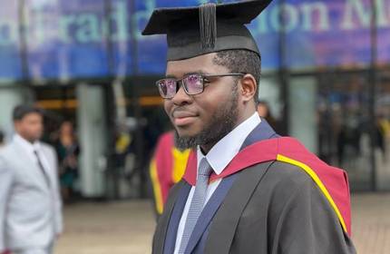 Olugbenga Adesanya stands wearing their graduate cap and gown during Graduation day