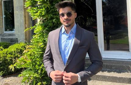 Vartesh Kumar, wearing a blue shirt and sunglasses, buttons his suit jacket