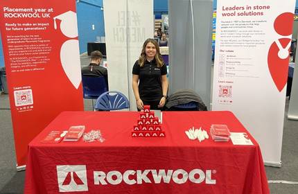 A young woman stands between two chairs at an information booth with red deocration