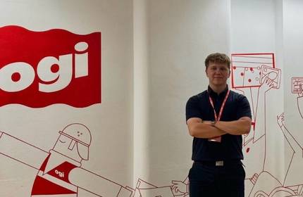 A young man stands with arms crossed in front of a branded wall with red decals