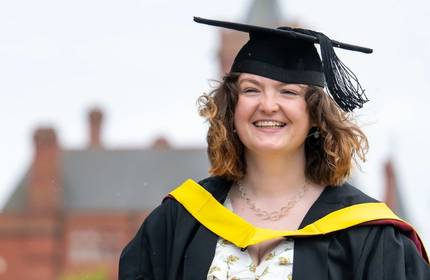 A smiling woman wearing a graduation gown, celebrating her achievement on graduation day.