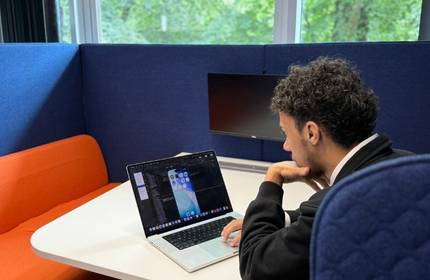 A young adult sits in a work booth at their laptop