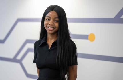 Elizabeth Aluko stands in front of a white wall with purple decorations
