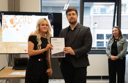 A woman in a dress receives an award from a man in a black dress