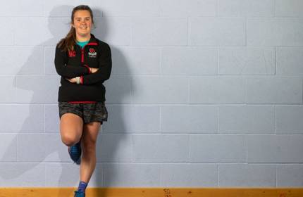 Naomi Davies stands leaning against a grey wall