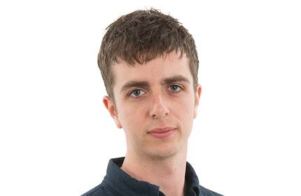 A headshot of a young man, wearing a blue polo shirt, in front of a white background