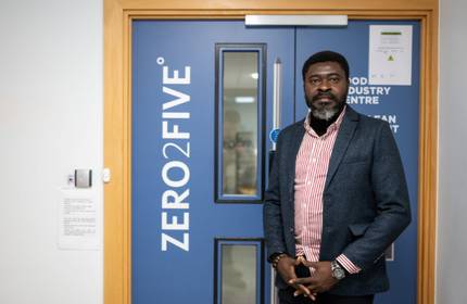 A person stands in front of a blue door. On the door is a sign that says ZERO2FIVE.