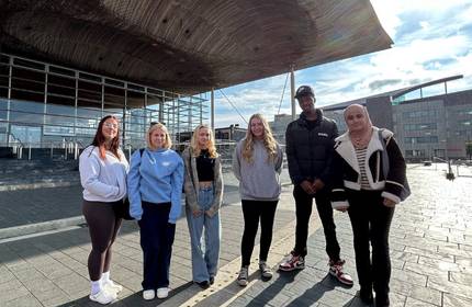 A group of people stand outside the the Senedd in Cardiff Bay.