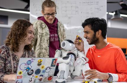 A group of people gathered around a small humanoid robot. One person is holding a screwdriver in their hand.