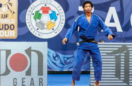 A young man wearing a dark blue judo suit with black belt.