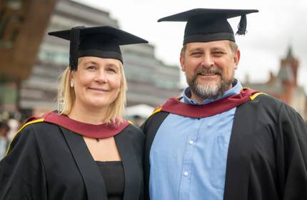 A man and woman in graduation caps and gowns stand side by side.
