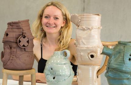 A person sits at a table. Arranged in front of them are four ceramic vases in a variety of colours.