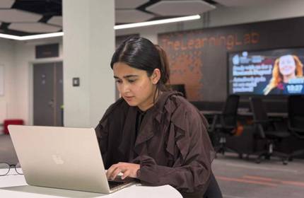 A person sits a round table, working intently at a laptop computer.