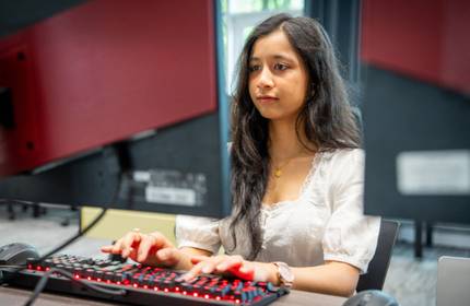 A young woman using a computer workstation types on an keyboard with illuminated red keys.