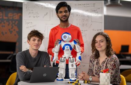 A person steadies a small humanoid robot that is standing on round table.
