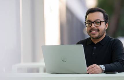 A person sits at a table. In front of them is a laptop computer.