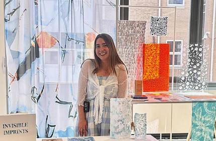A young woman stands next to a display of fabrics and textile prints.