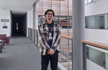 A man stands on a balcony in a bright atrium space.