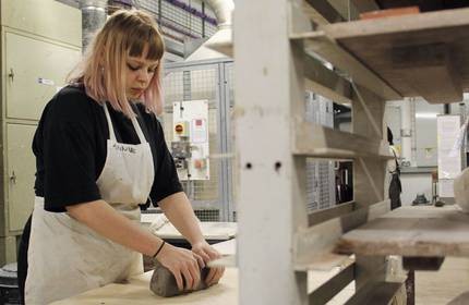 A person wearing an apron moulds a large piece of clay on a table