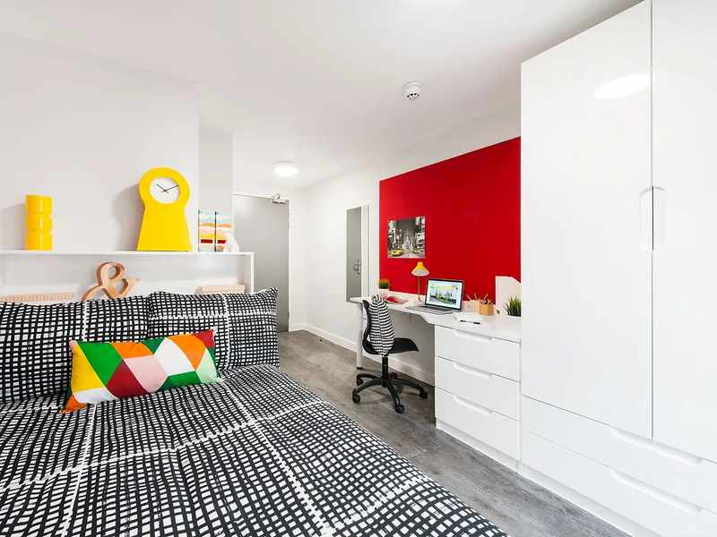 A bright, student accommodation room with bed, desk and wardrobe